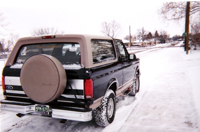 1996 Ford Bronco parked on a snowy street, rear view with spare tire cover