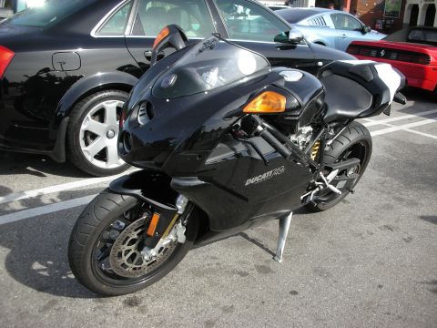 1998 Ford Crown Victoria - black Ducati 749 sportbike on a stand in a parking lot beside dark cars.