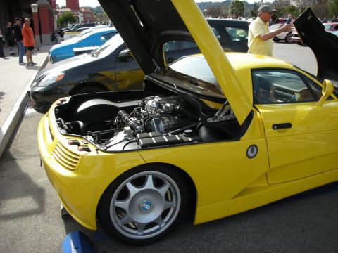 1998 Ford Crown Victoria - yellow mid-engine sports car with its front hood raised, parked at an outdoor car show.