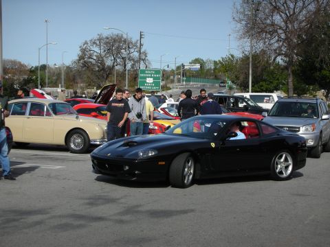 1998 Ford Crown Victoria - black Ferrari 550 Maranello coupe parked among classic cars at a busy outdoor car show.