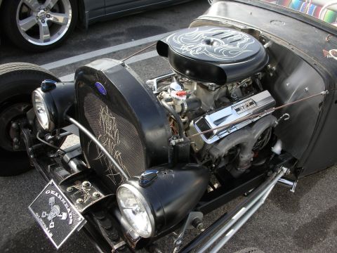 1998 Ford Crown Victoria - Close-up of a chrome V8 engine in a flat-black hot rod, with pinstriped covers and a skull-themed plaque.