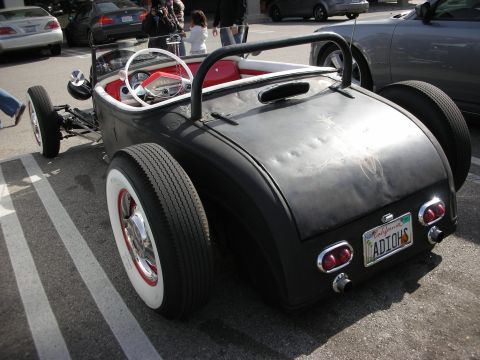 1998 Ford Crown Victoria - Rear view of a flat-black hot rod roadster with whitewall tires and a California license plate reading ADIOS.