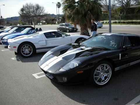 1998 Ford Crown Victoria - black Ford GT with silver stripes beside a white Ford GT, parked at an outdoor car show.