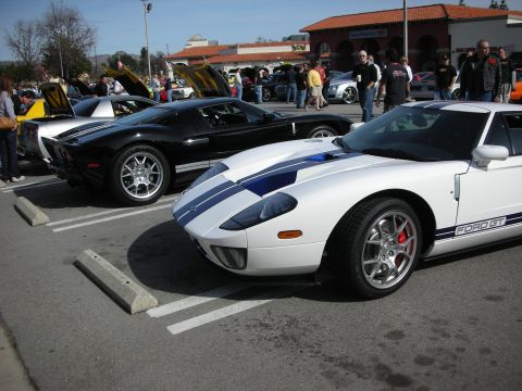 1998 Ford Crown Victoria - white Ford GT with blue racing stripes parked nose-out beside a black Ford GT at a crowded outdoor car show.
