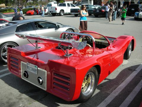 1998 Ford Crown Victoria - red open-cockpit Can-Am style race car shown from the rear, with a tall rear wing and a 'M8 CANAM' plate, at a car show.
