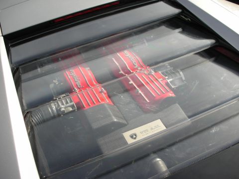 1998 Ford Crown Victoria - View through a glass engine cover of a Lamborghini V12 with red 'Lamborghini' cam covers and a crest plaque.