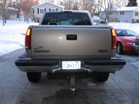 1998 GMC Sierra 1500 - The rear of a 1998 GMC Sierra 1500 pickup truck is shown in a snowy driveway with another vehicle visible.