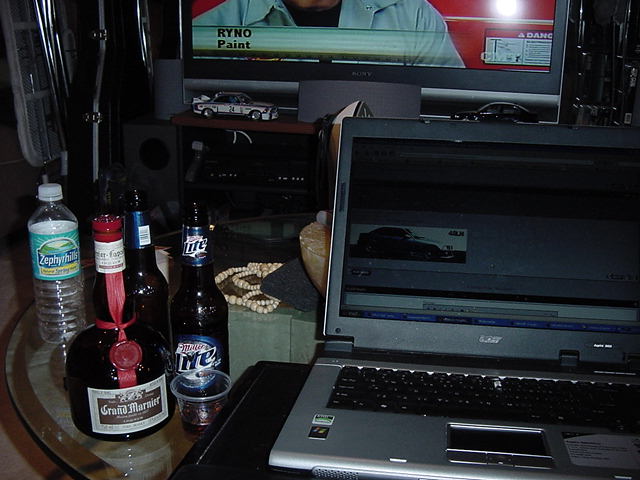 Table with liquor bottles, laptop, and TV showing a car in a dim room