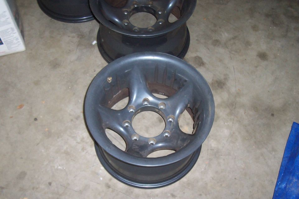 Several dark gray aftermarket truck wheels stacked on a concrete floor