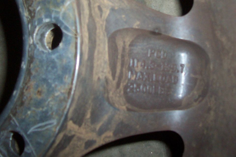 Close-up of a rusty metal wheel rim with stamped text indicating PCD 110.5-139.7 and MAX LOAD 2500 LBS
