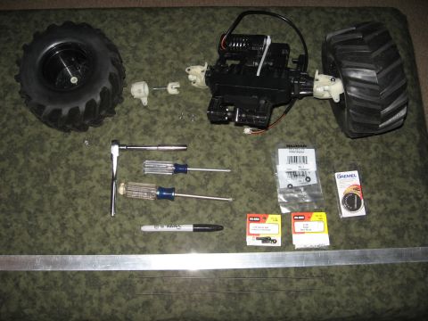 1990 Ford Bronco - RC car parts laid out with tools including screwdrivers, a ratchet, and a marker, alongside various small components and a ruler.