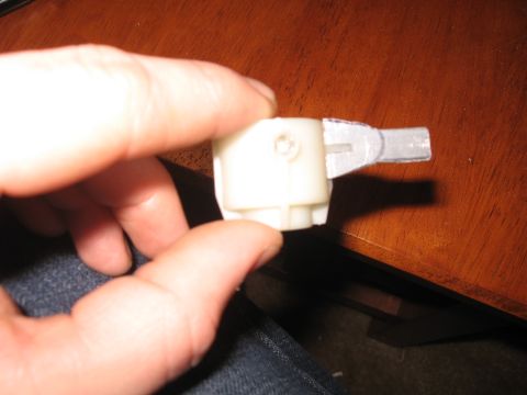 1990 Ford Bronco - A close-up view of a white plastic component with a metallic appendage, held by a person's hands.