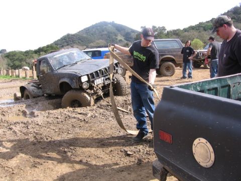 1989 Ford Bronco - A group of people are attempting to pull a mud-stuck truck out of a mire with a tow strap.