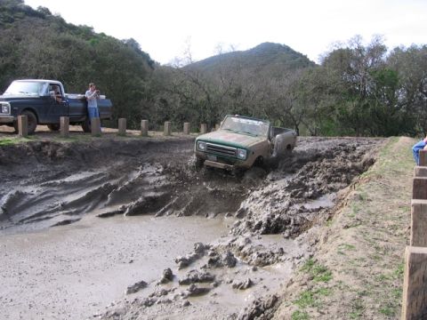 1989 Ford Bronco - An off-road vehicle navigates a challenging mud pit, while another truck waits on the side.