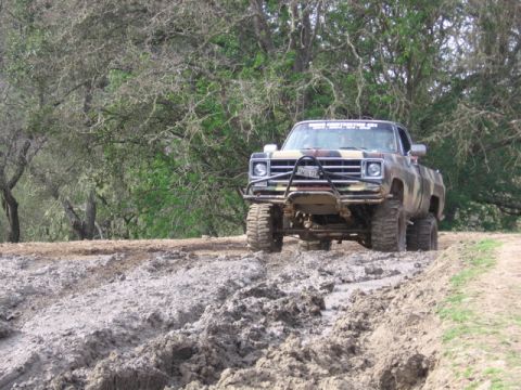 1989 Ford Bronco - A heavily modified pickup truck navigates a muddy track surrounded by trees.