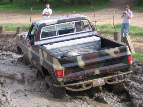 1989 Ford Bronco - A camouflage pickup truck navigates a muddy obstacle course, with onlookers observing the challenging terrain.