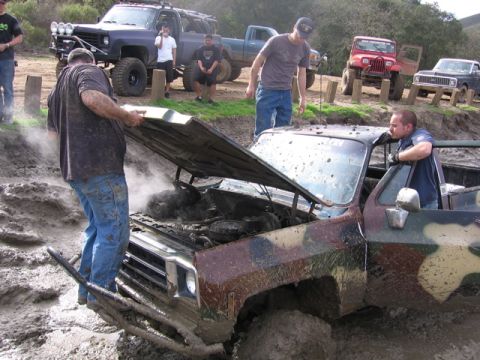 1989 Ford Bronco - Muddy pickup truck with hood open, steam rising from engine. Other off-road vehicles and people are present.