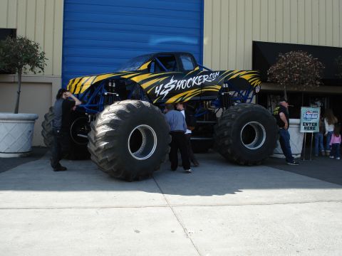 1994 Ford Bronco - A monster truck with a distinctive yellow and black tiger stripe paint scheme is parked outside a building.