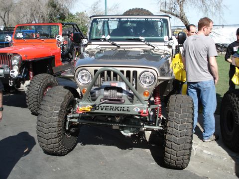 1994 Ford Bronco - Two modified Jeeps are parked side-by-side, one in tan and grey, the other in orange, with large off-road tires.