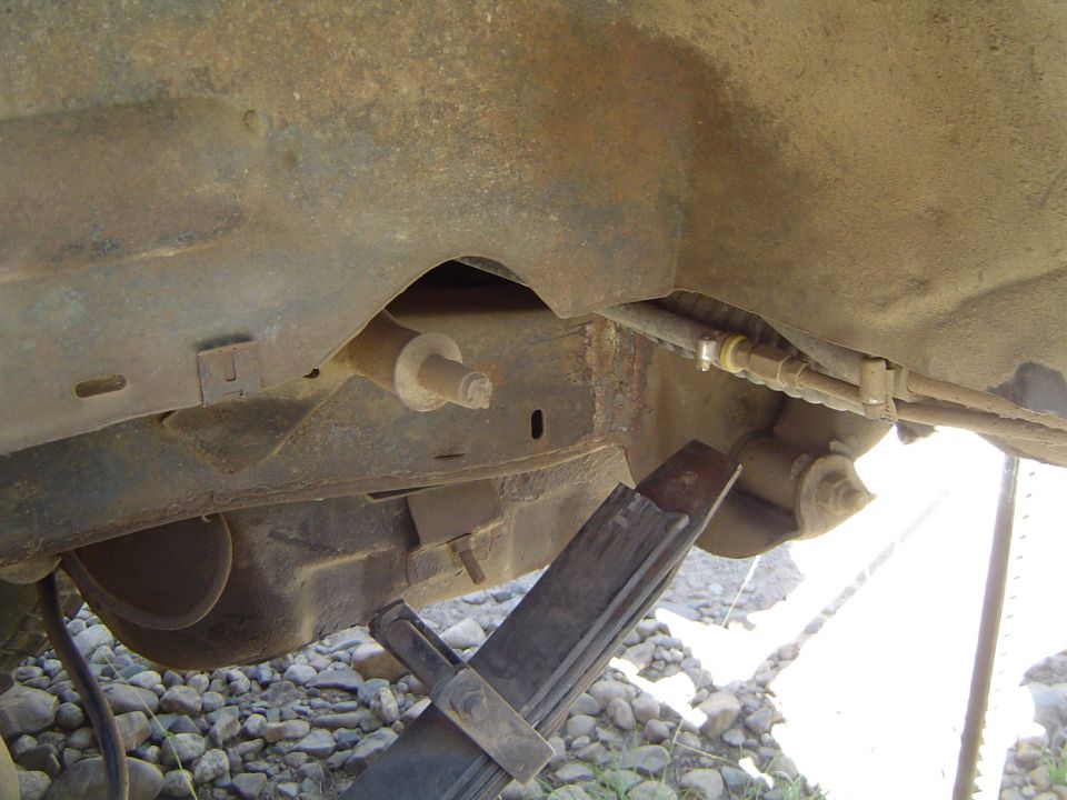 Rusty frame rail, crossmember and shackle mount seen from under a vehicle on a jack