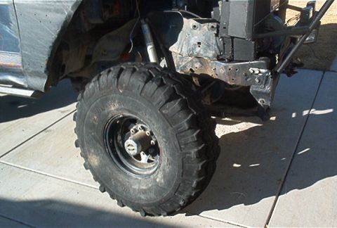 1986 Ford Bronco - Close-up of a heavily modified vehicle's front wheel and exposed frame, suggesting off-road use.