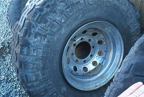 1986 Ford Bronco - A close-up view of a off-road tire and its metal rim, resting on gravel.