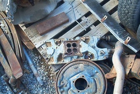 1986 Ford Bronco - Assorted automotive parts including an intake manifold and brake drum are piled on a wooden pallet.