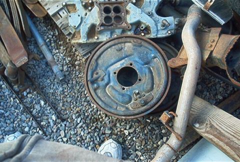 1986 Ford Bronco - Various automotive parts, including an engine manifold and brake drum, are scattered on a gravel surface.