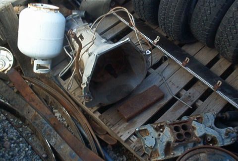 1986 Ford Bronco - Assorted automotive parts and scrap metal piled on wooden pallets.