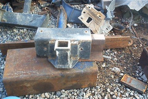 1986 Ford Bronco - A rusty trailer hitch receiver is shown in a pile of scrap metal and vehicle parts.