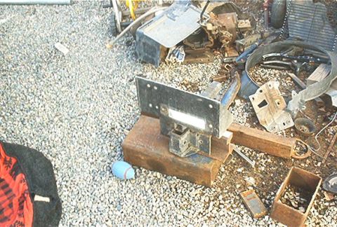 1986 Ford Bronco - A collection of scrap metal parts and a hitch receiver bracket are scattered on a gravel surface.