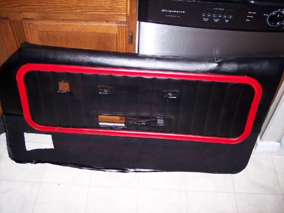 Black vinyl door panel with red trim ring leaning against kitchen cabinets and dishwasher