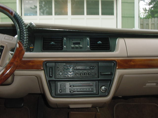 Tan sedan dashboard with wood trim, aftermarket stereo and equalizer stacked in center