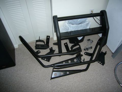 2000 Ford Crown Victoria - A black bull bar and its associated mounting brackets and hardware are disassembled and spread across a carpeted floor.