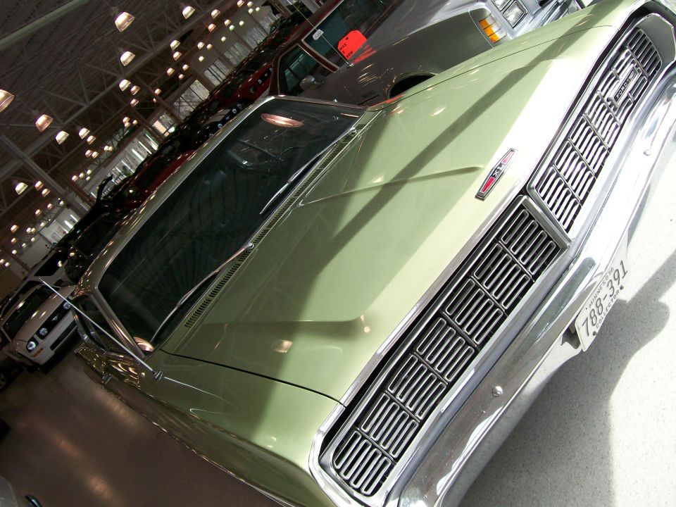 Light green 1967 Ford car front grille and hood detail, with other cars visible behind