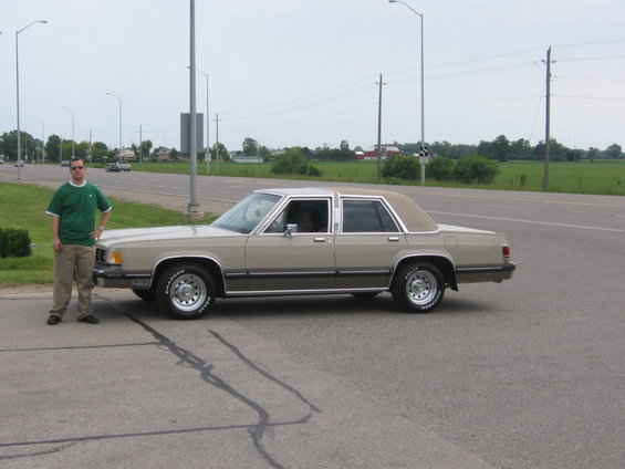 Side profile of a tan Mercury Grand Marquis sedan with a man standing beside it