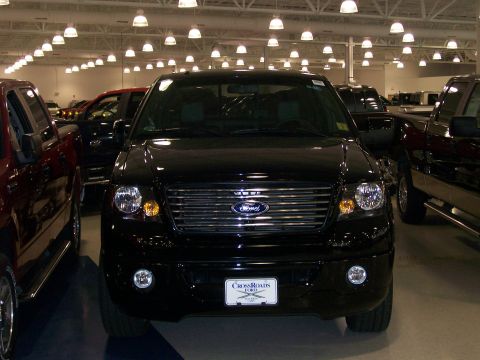 1996 Ford Bronco - A black Ford F-150 pickup truck is parked in a showroom with other vehicles under bright lights.