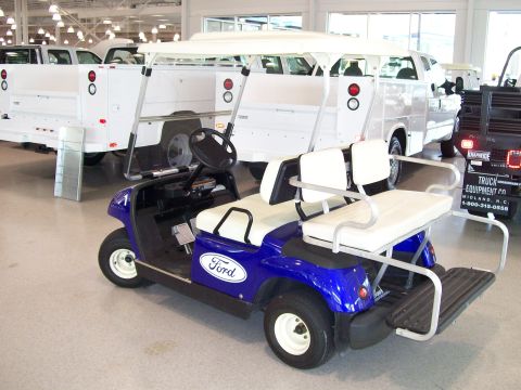 1996 Ford Bronco - A blue Ford golf cart is parked inside a building with several white trucks visible in the background.