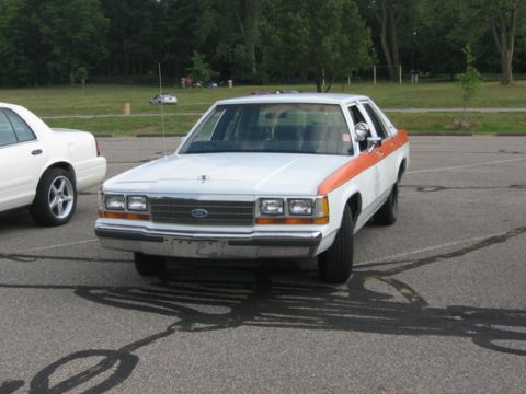 1988 Mercury Grand Marquis - A 1988 Mercury Grand Marquis is parked in a lot, showing its front end and distinctive orange side stripe.