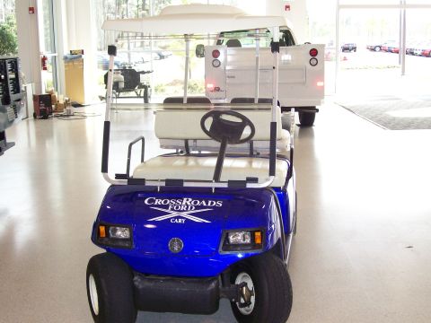 1996 Ford Bronco - A blue golf cart is parked inside a dealership, with a white truck visible in the background.