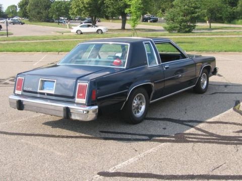 1988 Mercury Grand Marquis - Rear view of a dark blue coupe parked in an asphalt lot with trees and other cars in the background.
