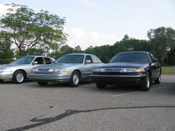 Three Ford Crown Victorias parked in a lot, two silver and one black