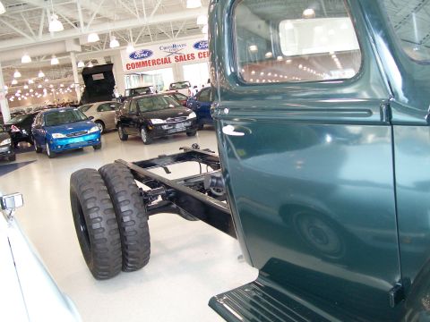 1996 Ford Bronco - Chassis of a truck with dual rear wheels displayed in a car dealership showroom.
