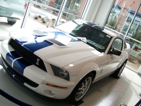 1996 Ford Bronco - A white Ford Mustang Shelby GT500 with blue racing stripes is displayed indoors.