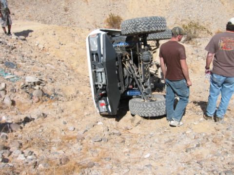 1997 Ford Ranger - An off-road vehicle lies on its side in a dusty, rocky terrain, with two men observing the scene.
