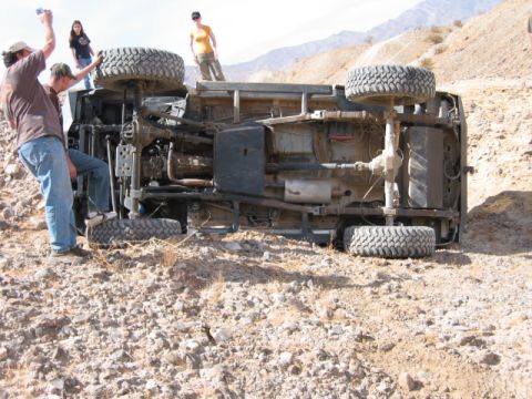 1997 Ford Ranger - An off-road vehicle lies on its side in a rocky, desert environment, with several people observing the scene.