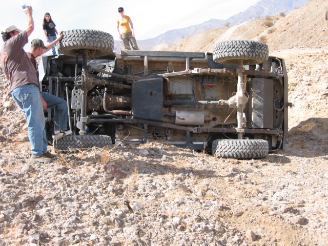 Overturned off-road vehicle on rocky terrain with people standing around