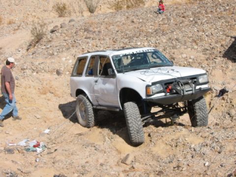 1997 Ford Ranger - A white off-road SUV with significant damage and modifications is stuck on a rocky incline.