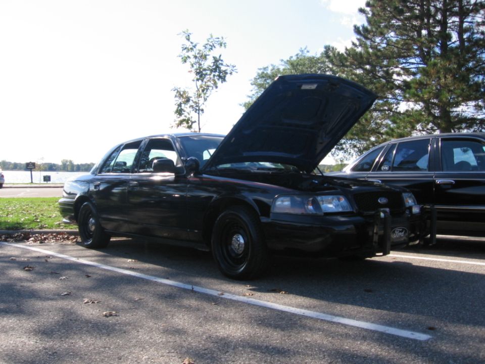 Black police car with hood open, parked next to another dark sedan