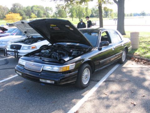 1988 Mercury Grand Marquis - A black 1988 Mercury Grand Marquis is displayed with its hood open, parked alongside other vehicles at an outdoor event.